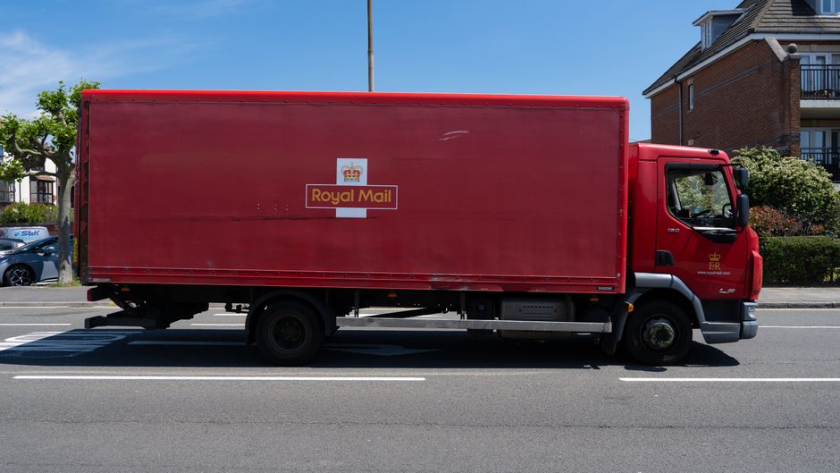 A red Royal Mail delivery truck parked on a street in daylight, with a floral arrangement visible through the open side door of the truck. The truck features the Royal Mail logo and is situated in a r