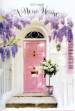 A doorway in Shadwell is shown as a gentle vignette of new-home joy, wrapped in soft pastels and natural texture. The focal point is a light pink front door, painted in a smooth, calming shade that stands out quietly against a backdrop of whitewashed masonry. The finish of the door has a subtle sheen, catching the kind of light you might find drifting in from the riverside walks near Shadwell Basin. Overhead, wisteria cascades in trailing strands of lavender and muted violet, its blossoms gathered into graceful plumes that drape over the door frame, turning the entrance into a kind of floral archway. A single shutter painted in coordinating pastel sits alongside, reinforcing the gentle, cohesive palette of the façade. At the doorstep, a metal bucket in a soft grey tone rests solidly on the paving, its simple, utilitarian form made tender by the blooms it contains. Emerging from the bucket is a generous bouquet of creamy white roses, their velvety petals tightly layered and slightly ruffled at the edges, each flower suggesting freshness and careful handling. Sprigs of soft green foliage weave through the arrangement, adding a natural, airy feel that lightens the ivory tones. A delicate pink ribbon is tied around the bucket, its bow loose and elegant, trailing slightly as if stirred by a faint dockside breeze. The entire scene feels composed yet effortless, like a real Shadwell doorstep prepared by someone who loves both their flowers and their home. It's an image that speaks of a housewarming or congratulations, aligning perfectly with the sentiment of a card that wishes comfort, optimism, and a warm welcome to life in this quietly historic part of East London.